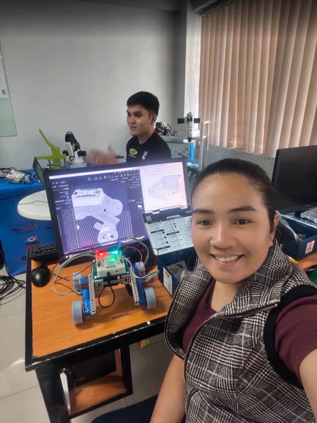 Kat Hervera with a mobile robot, electronics, and a digital 3D model in the robotics lab